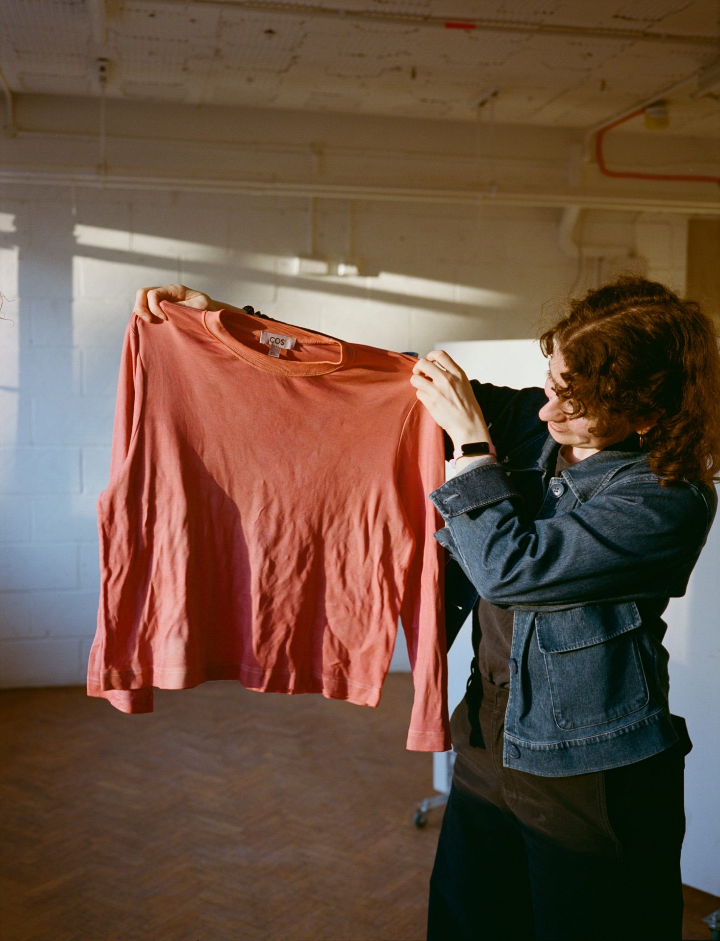 Participant holds a top they dyed with madder, sunlight streaming through a window behind them.