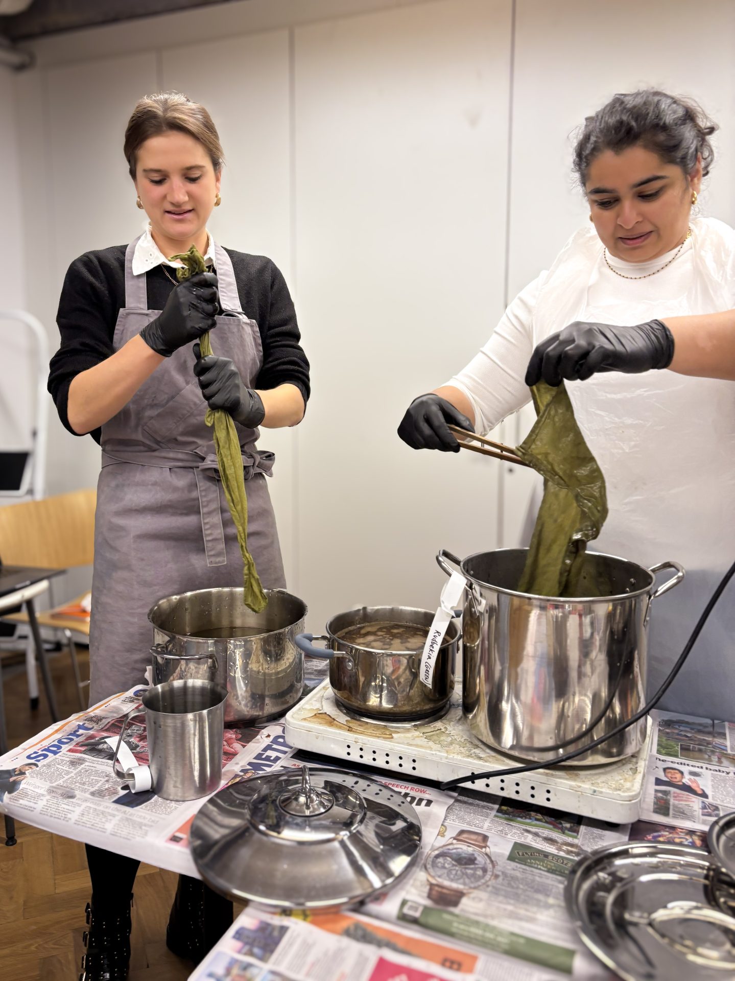 Two people squeeze excess liquid from their green‑dyed bandanas after the dye bath