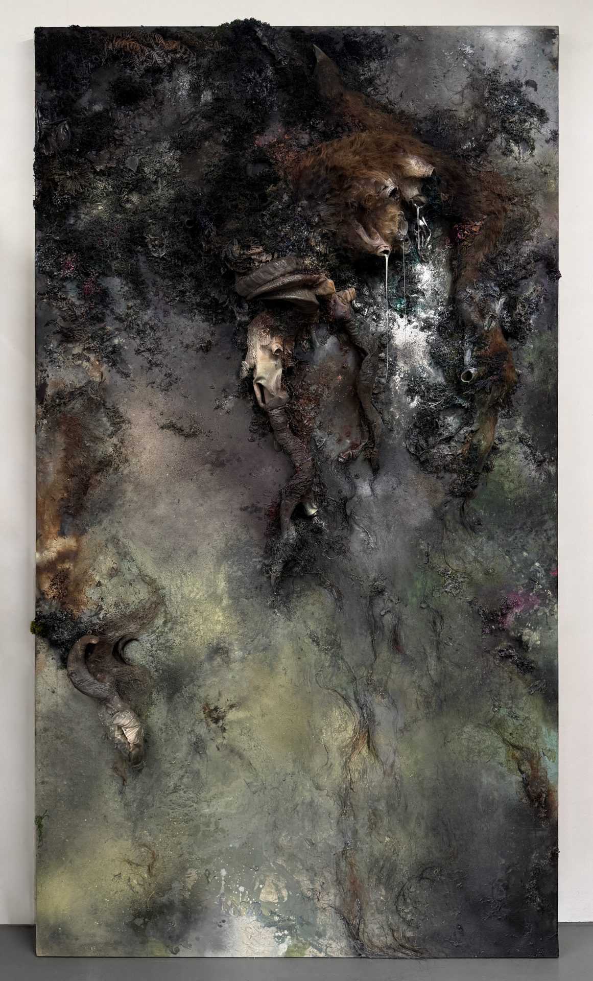 Large sculptural wall painting with a dark, textured surface combining human hair, deer taxidermy, plastic waste and reflective materials.