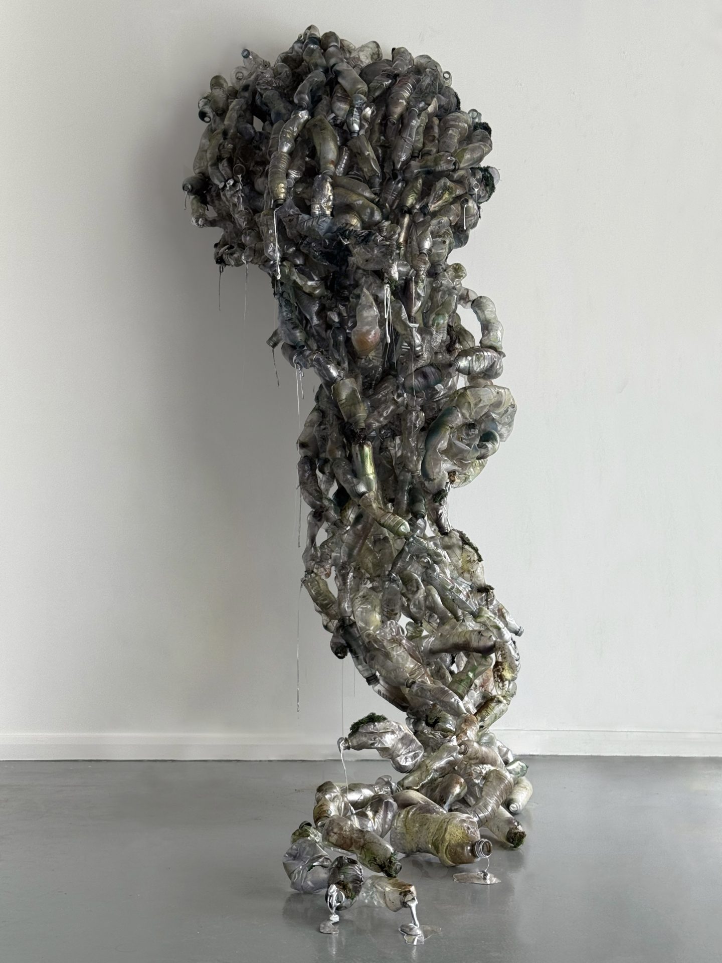 Suspended sculptural form made from discarded plastic bottles and translucent synthetic material, with reflective silver surfaces.”